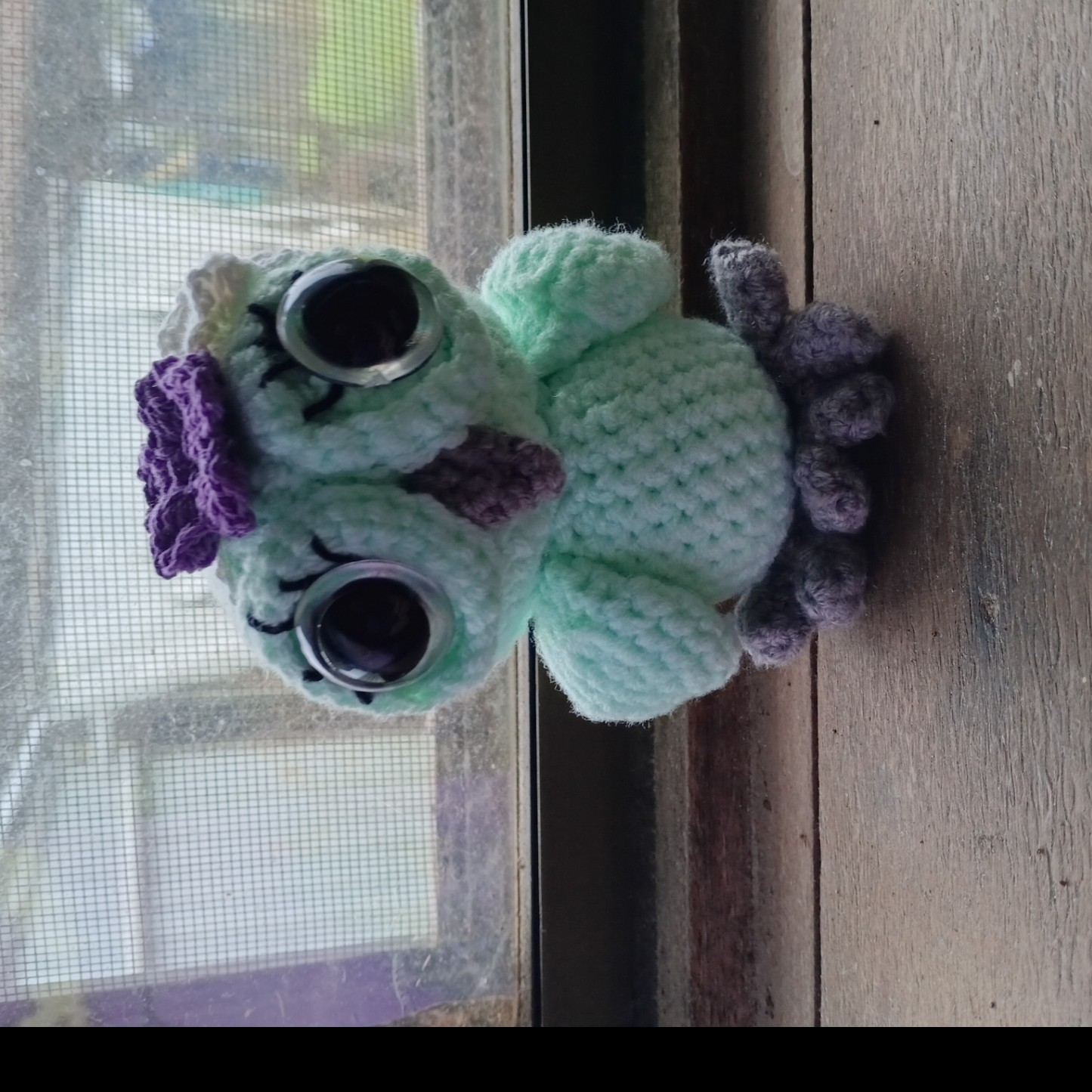 A mint green crocheted owl with a purple flower crown